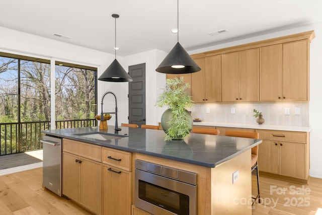 kitchen featuring a kitchen island with sink, stainless steel microwave, a sink, and visible vents