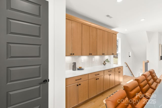 kitchen with light wood finished floors, recessed lighting, light countertops, visible vents, and backsplash