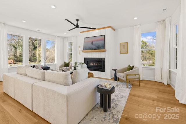 living room featuring a glass covered fireplace, ceiling fan, light wood-style flooring, and recessed lighting