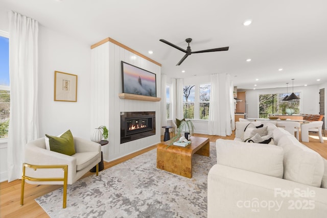 living area with a glass covered fireplace, ceiling fan, recessed lighting, and wood finished floors