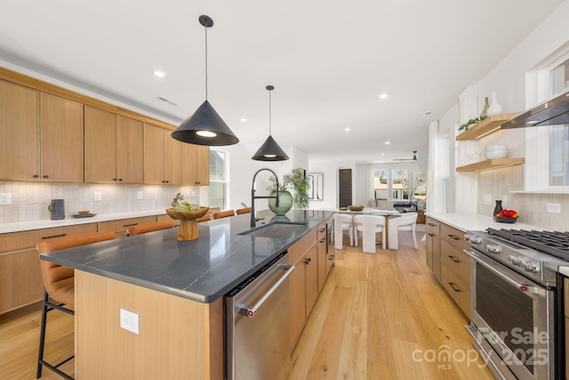 kitchen featuring a center island with sink, light wood finished floors, appliances with stainless steel finishes, a sink, and a kitchen breakfast bar