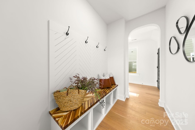 mudroom with light wood finished floors, baseboards, and arched walkways