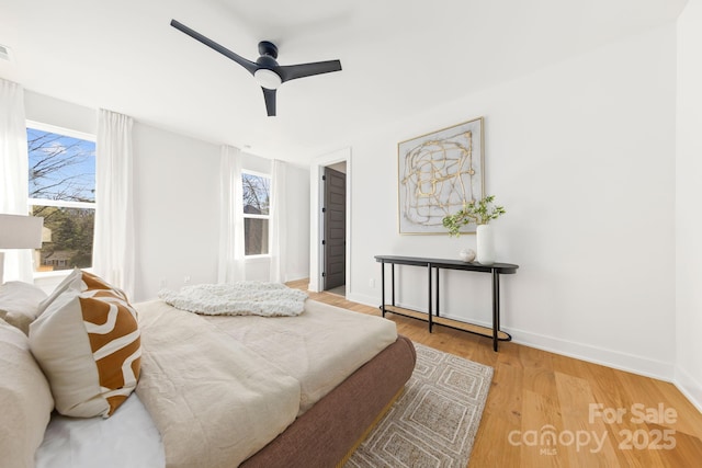 bedroom featuring ceiling fan, multiple windows, baseboards, and wood finished floors