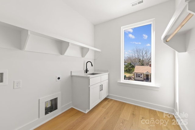 washroom featuring baseboards, visible vents, a sink, and light wood finished floors