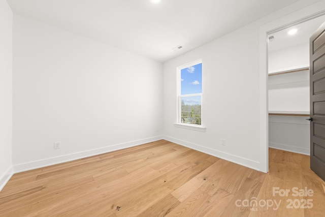 unfurnished bedroom with baseboards, a closet, a walk in closet, and light wood-style floors