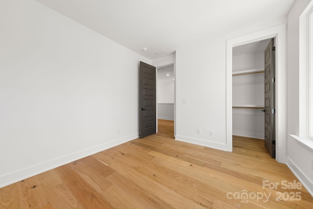 unfurnished bedroom featuring a closet, light wood-style flooring, baseboards, and a spacious closet