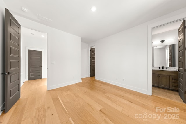 unfurnished bedroom with ensuite bathroom, light wood-type flooring, a sink, and baseboards