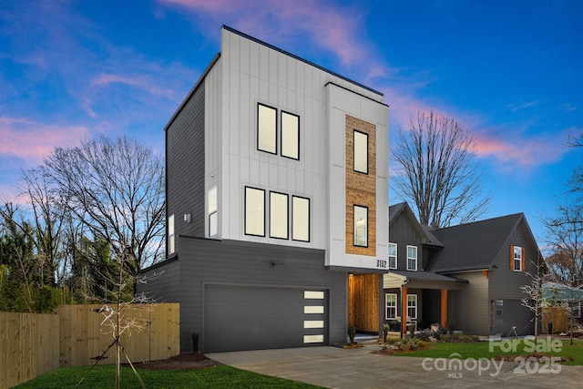 modern home featuring driveway, board and batten siding, an attached garage, and fence