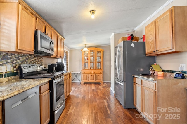 kitchen featuring tasteful backsplash, ornamental molding, light stone counters, stainless steel appliances, and dark wood-type flooring