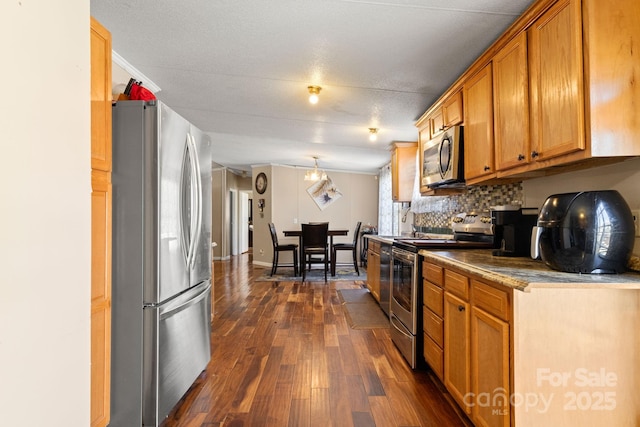 kitchen featuring dark wood-type flooring, lofted ceiling, appliances with stainless steel finishes, and tasteful backsplash