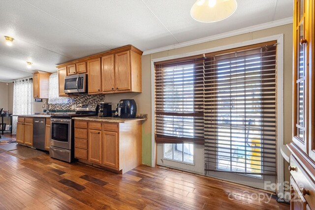 kitchen with a healthy amount of sunlight, appliances with stainless steel finishes, dark hardwood / wood-style floors, and ornamental molding