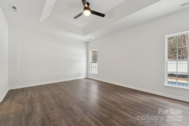 empty room with ceiling fan, a tray ceiling, and dark hardwood / wood-style flooring