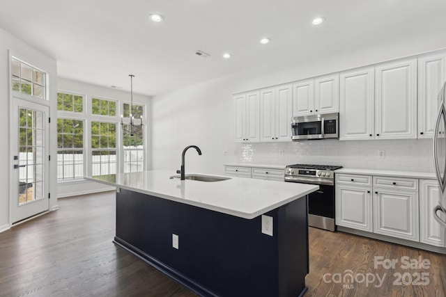 kitchen with sink, stainless steel appliances, white cabinets, a center island with sink, and decorative light fixtures