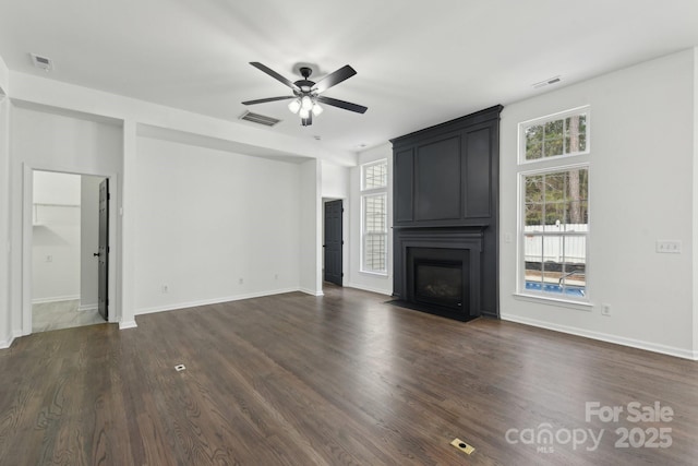 unfurnished living room with a healthy amount of sunlight, a large fireplace, dark wood-type flooring, and ceiling fan