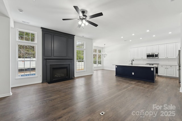 unfurnished living room with sink, dark hardwood / wood-style floors, ceiling fan with notable chandelier, and a large fireplace