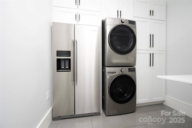 clothes washing area with stacked washer / dryer, light tile patterned floors, and cabinets