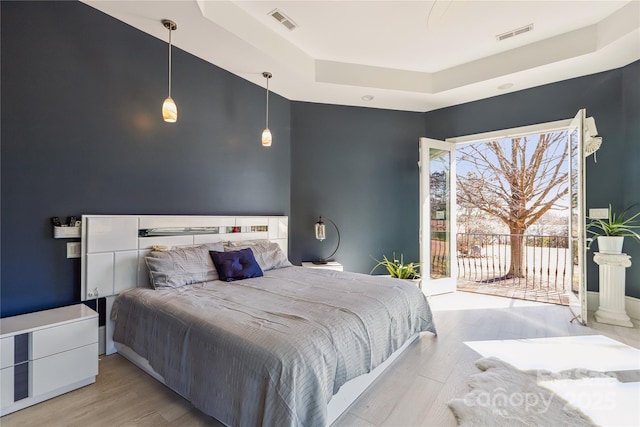 bedroom with a raised ceiling, access to exterior, and light hardwood / wood-style flooring