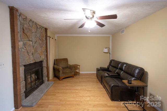 living room featuring ceiling fan, a textured ceiling, a fireplace, and light hardwood / wood-style floors