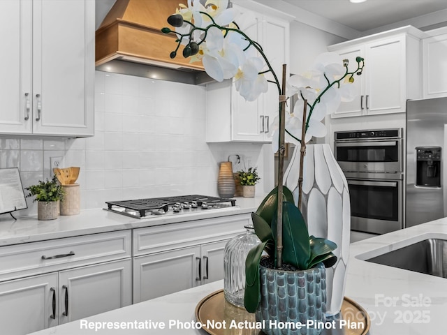 kitchen with backsplash, appliances with stainless steel finishes, premium range hood, and white cabinets