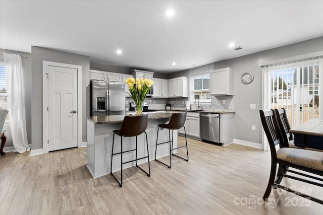 kitchen with a kitchen island, tasteful backsplash, white cabinets, dark stone counters, and stainless steel appliances