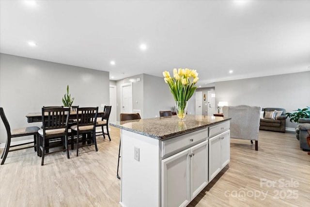 kitchen with white cabinetry, a center island, light hardwood / wood-style flooring, dark stone countertops, and a kitchen breakfast bar