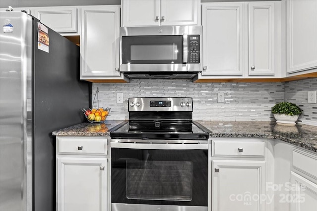 kitchen featuring stainless steel appliances, dark stone countertops, white cabinets, and backsplash