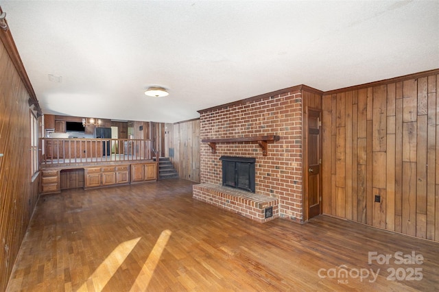 unfurnished living room with crown molding, dark wood-type flooring, a fireplace, and wood walls