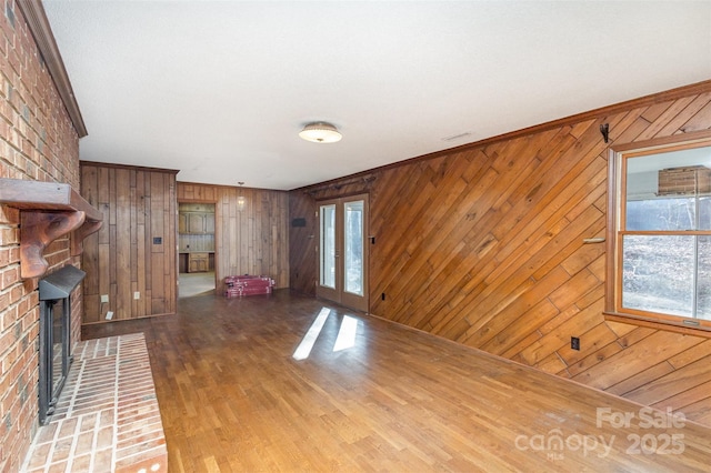 unfurnished living room with ornamental molding, a brick fireplace, hardwood / wood-style floors, and french doors