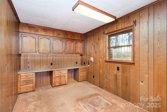 home office featuring light carpet, built in desk, and wood walls