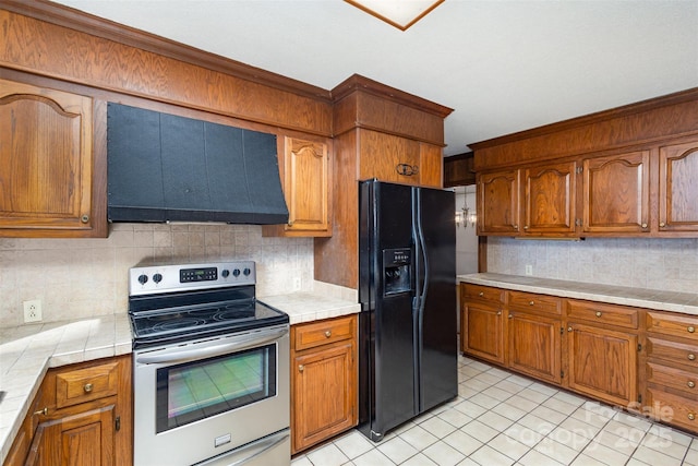 kitchen with stainless steel electric stove, range hood, tasteful backsplash, tile counters, and black fridge with ice dispenser