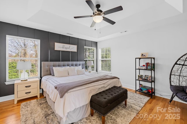 bedroom featuring ceiling fan, a raised ceiling, and light wood-type flooring