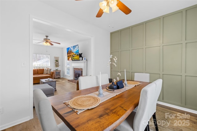 dining area with ceiling fan, wood-type flooring, and a brick fireplace