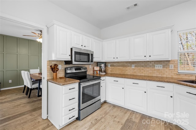 kitchen with white cabinetry, stainless steel appliances, light hardwood / wood-style floors, and dark stone countertops