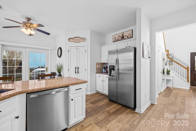 kitchen with stainless steel appliances, light wood-type flooring, white cabinets, and light stone counters