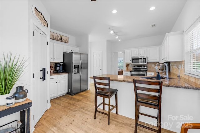 kitchen featuring stainless steel appliances, white cabinets, a kitchen bar, and dark stone counters