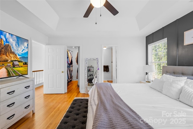 bedroom featuring a walk in closet, a raised ceiling, a closet, and light wood-type flooring