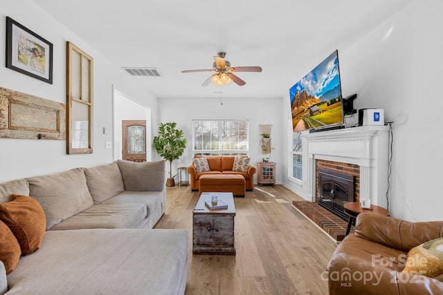 living room with a brick fireplace, light hardwood / wood-style flooring, and ceiling fan