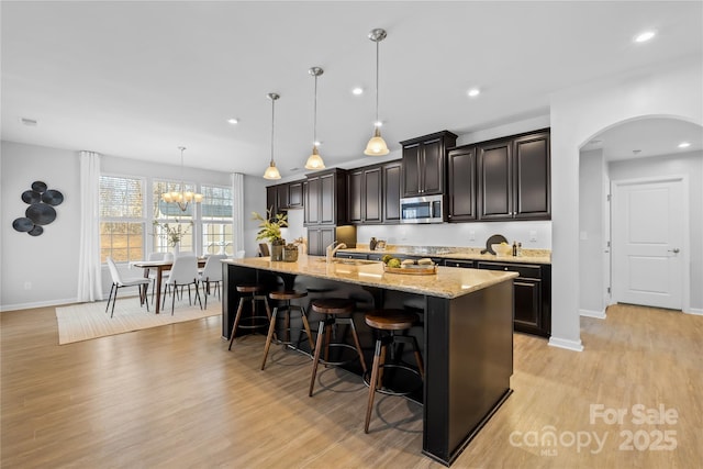 kitchen with pendant lighting, a breakfast bar area, a kitchen island with sink, dark brown cabinetry, and light hardwood / wood-style flooring