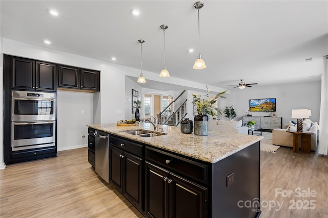 kitchen with sink, light stone counters, an island with sink, pendant lighting, and stainless steel appliances