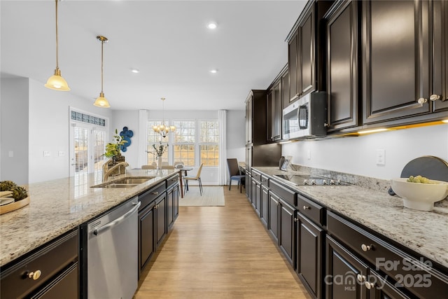 kitchen with sink, hanging light fixtures, light stone counters, stainless steel appliances, and dark brown cabinets