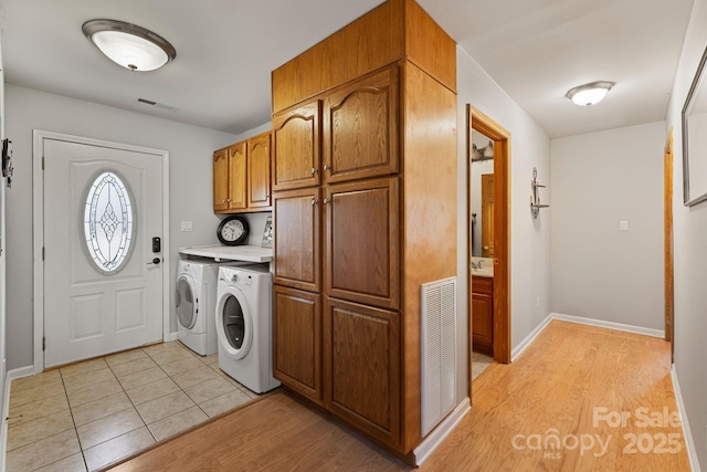 clothes washing area with independent washer and dryer, light hardwood / wood-style floors, and cabinets