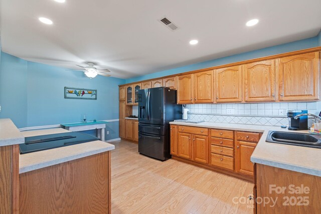 kitchen featuring light hardwood / wood-style floors, black fridge with ice dispenser, sink, and decorative backsplash