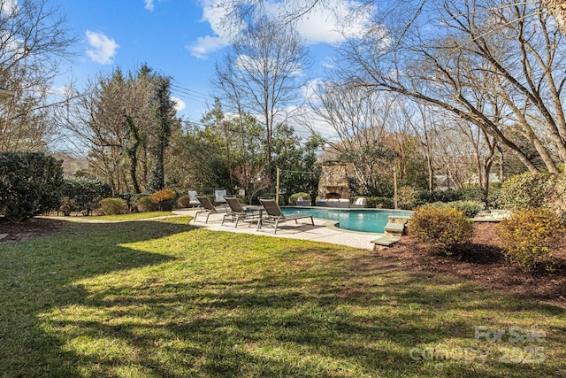 view of swimming pool with a yard, an outdoor stone fireplace, and a patio area