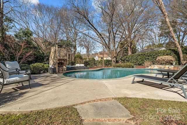 view of swimming pool featuring a patio and an outdoor stone fireplace