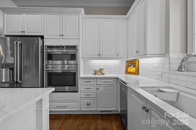 kitchen with appliances with stainless steel finishes, light stone countertops, sink, and white cabinets