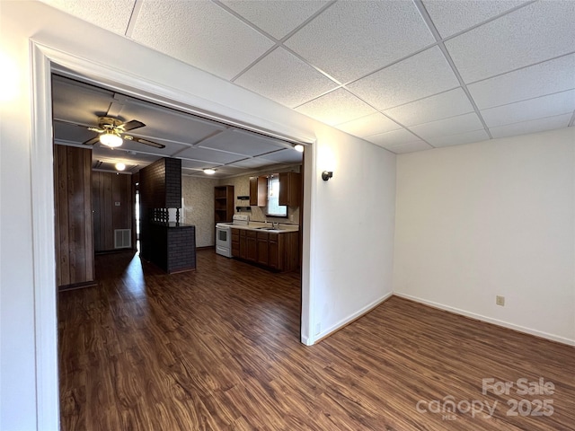 unfurnished living room with sink, dark wood-type flooring, ceiling fan, and a paneled ceiling