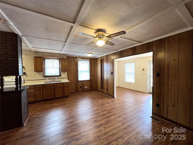 kitchen featuring sink, coffered ceiling, a textured ceiling, dark hardwood / wood-style flooring, and wood walls