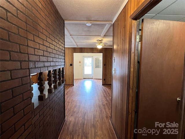 hall featuring hardwood / wood-style flooring, wooden walls, a textured ceiling, and brick wall