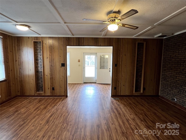 interior space featuring dark wood-type flooring, wood walls, a textured ceiling, ceiling fan, and brick wall