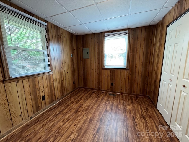 spare room with dark wood-type flooring, a drop ceiling, and wood walls